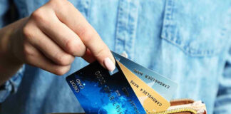 Hand holding credit cards over a brown purse