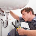 A plumber working under a sink with tools