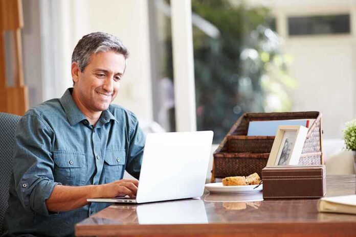 A man sitting at a desk working on a laptop with a smile