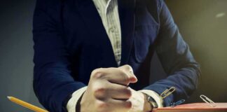 A man's clenched fist resting on a desk with office supplies nearby