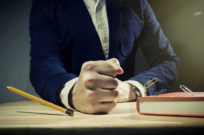 shutterstock_482144998.jpg A man's clenched fist resting on a desk with office supplies nearby