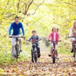 A family of four riding bicycles on a leafy path during autumn