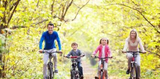 A family of four riding bicycles on a leafy path during autumn