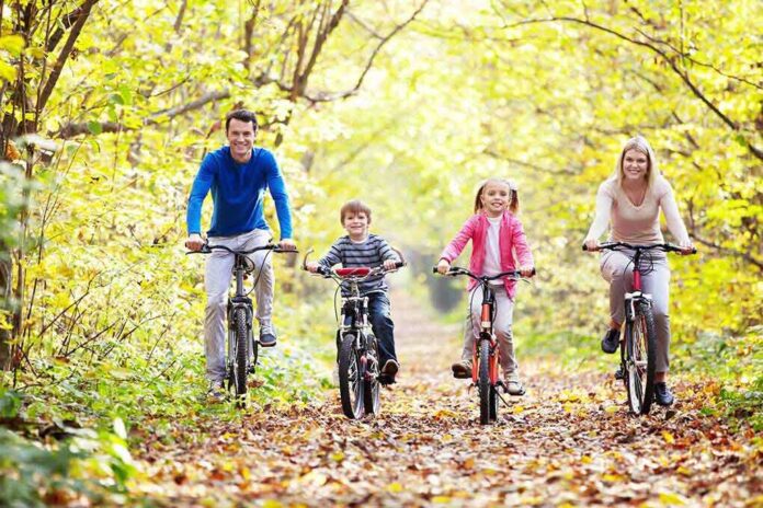 A family of four riding bicycles on a leafy path during autumn