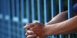 Close up of clasped hands resting on a blue fence
