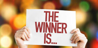 Hands holding a sign reading The Winner Is...