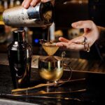 Bartender pouring a cocktail through a strainer into a gold cup
