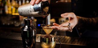 Bartender pouring a cocktail through a strainer into a gold cup