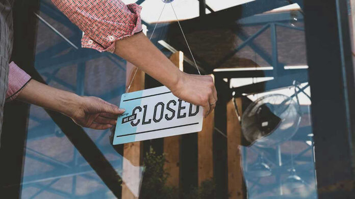 Hand placing closed sign on glass door
