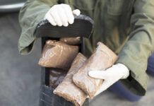 Person handling packages wearing gloves and green jacket.