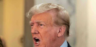 Man in suit with open mouth, speaking passionately.