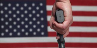 A hand holding a gun in front of an American flag