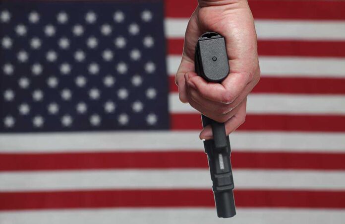 A hand holding a gun in front of an American flag