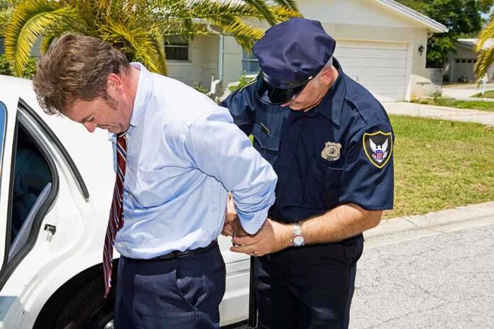 A police officer handcuffing a man in formal attire outside a police car