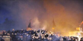 A large crowd of police officers in helmets facing a smoky protest scene at night