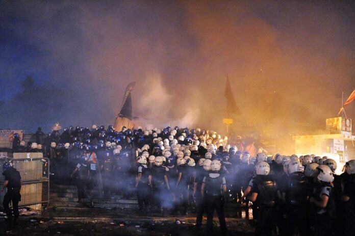 A large crowd of police officers in helmets facing a smoky protest scene at night