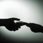 NYC’s Dark Side: Diamond Bribery Unveiled Silhouette of hands exchanging money in dim light.