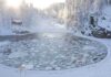A serene winter landscape featuring a frozen lake surrounded by snow-covered trees and a log cabin