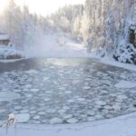 Ice CRACKS—Three Brothers Gone in Moments A serene winter landscape featuring a frozen lake surrounded by snow-covered trees and a log cabin