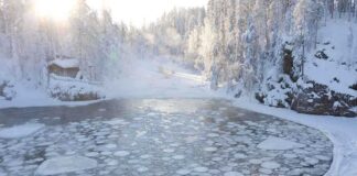 A serene winter landscape featuring a frozen lake surrounded by snow-covered trees and a log cabin