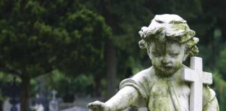 Weathered statue of a child angel holding a cross in a cemetery