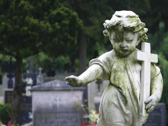 Weathered statue of a child angel holding a cross in a cemetery