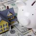 SHOCKING 45% Electric Price Spike Devastates Households A model house next to a white piggy bank on a bed of dollar bills