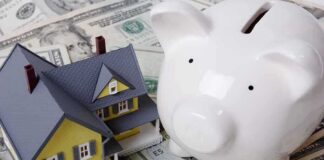 A model house next to a white piggy bank on a bed of dollar bills