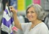 Senior woman smiling while holding a purple and gray shirt in a clothing store