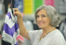Retail Apocalypse: Cost-of-Living Crisis Strikes Senior woman smiling while holding a purple and gray shirt in a clothing store