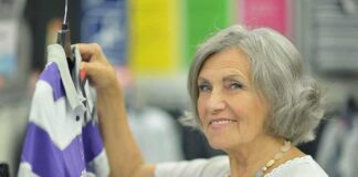 Senior woman smiling while holding a purple and gray shirt in a clothing store