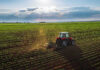 Tractor plowing a vast green field at sunset.