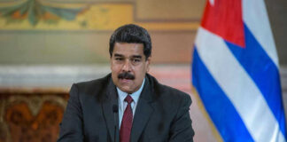 Man speaking at podium with Cuban flag in background.