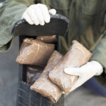 60 Pounds Hidden — Vetted Traveler’s Stunning Betrayal Person handling packages wearing gloves and green jacket.