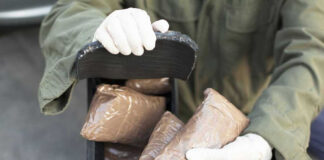 Person handling packages wearing gloves and green jacket.