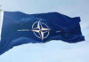 NATO flag waving against blue sky.