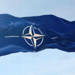 Closed-Door NATO Blowup Rocks Washington NATO flag waving against blue sky.