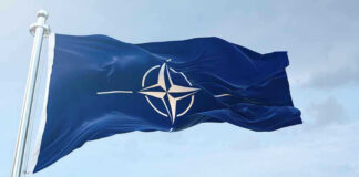 NATO flag waving against blue sky.