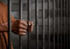 Hands gripping prison cell bars.