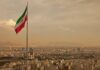 Iranian flag waving over a city skyline with mountains in the background