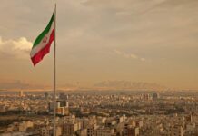 HUMAN CHILDREN SHIELDS Surround Iranian Power Plants Iranian flag waving over a city skyline with mountains in the background