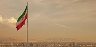 Iranian flag waving over a city skyline with mountains in the background