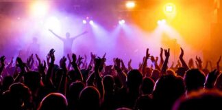 Crowd at a concert with raised hands and colorful stage lights