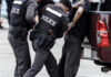Police officers arresting a handcuffed person.