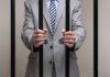 Doctor’s Shocking Act: Forced Abortion Pills Businessman in a suit holding prison bars with handcuffs on his wrists