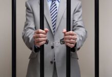 Doctor’s Shocking Act: Forced Abortion Pills Businessman in a suit holding prison bars with handcuffs on his wrists