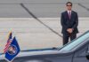 Kash Patel’s Quiet Funeral Turns into Public Spectacle A security officer in a suit stands guard near a presidential vehicle at an airport