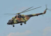 Apache Down Near Hormuz — What Hit It? Camouflage military helicopter in flight against blue sky.
