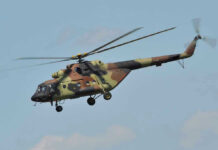 Apache Down Near Hormuz — What Hit It? Camouflage military helicopter in flight against blue sky.