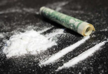 Powder lines, rolled dollar bill on black surface.